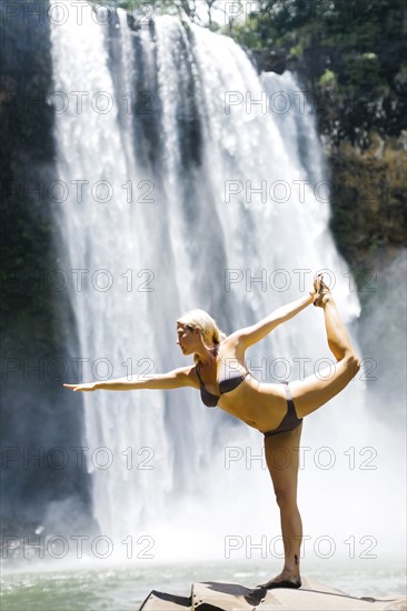 USA, Hawaii, Kauai, Woman practicing yoga next to waterfall