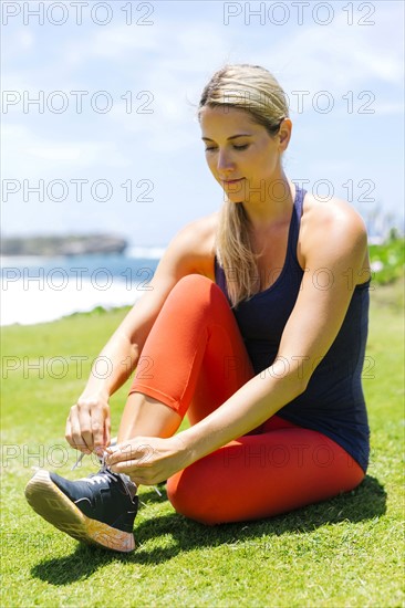 USA, Hawaii, Kauai, Woman sitting on lawn and lacing shoes