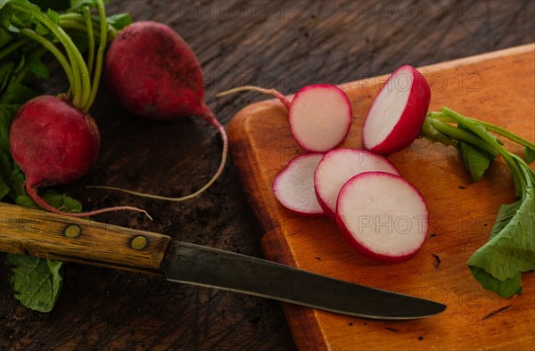 Slices of red radish and knife on cutting board