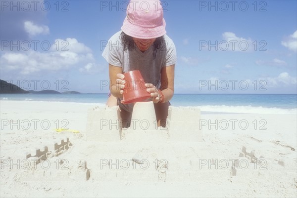 USA, USVI, St. John, Mature woman in pink sun hat making sandcastle on beach