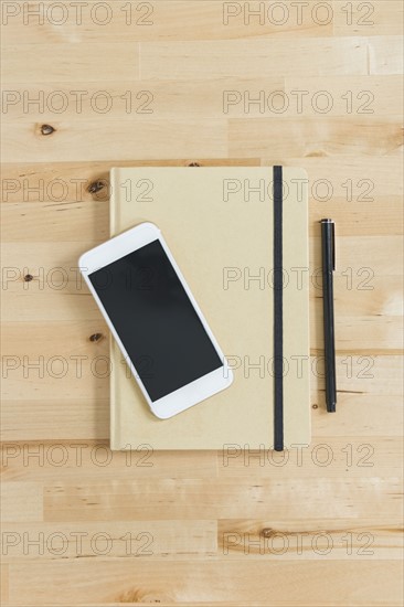 Directly above view of smart phone and personal organizer and pen on wooden desk