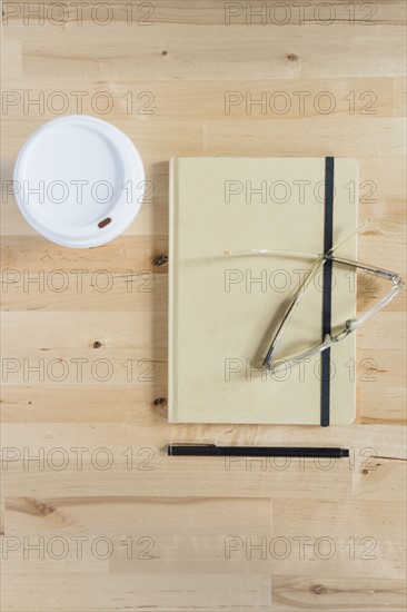 Disposable cup, diary, eyeglasses and pen on wooden desk