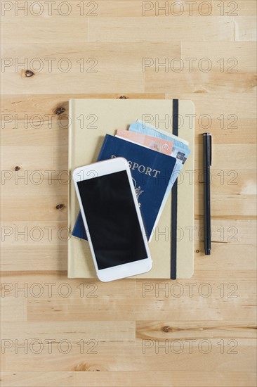 Diary, passport with paper currency, smart phone and pen on wooden table