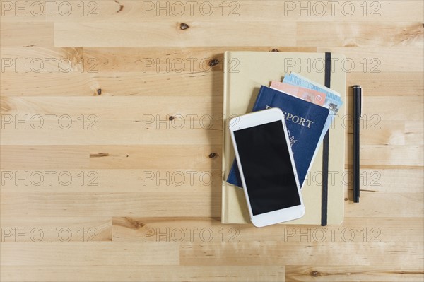 Diary, passport with paper currency, smart phone and pen on wooden table