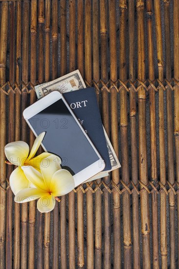 Passport with American money, smart phone and yellow plumeria flowers on bamboo mat