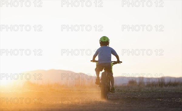 USA, Colorado, Rear view of boy (8-9) cycling at sunset