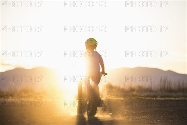 USA, Colorado, Rear view of boy (8-9) cycling at sunset