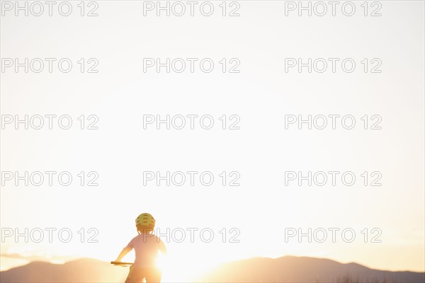 Rear view of boy (8-9) cycling at sunset