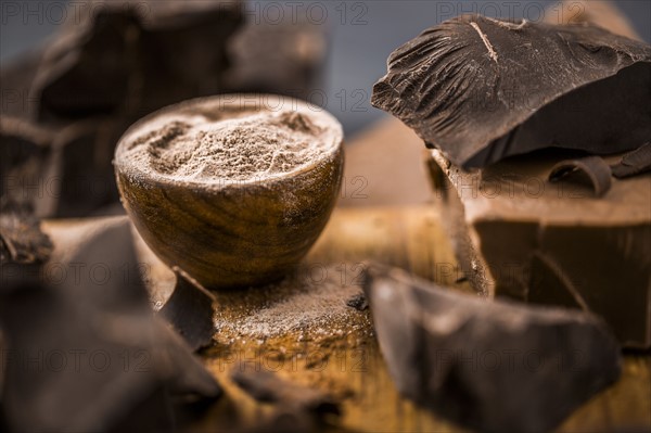 Ground chocolate in wooden bowl next to chunk of chocolate