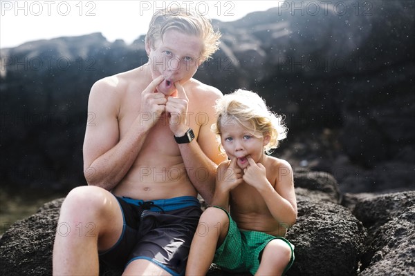 Young man with younger brother (4-5) sitting on rocks