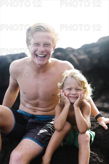 Young man with younger brother (4-5) sitting on rocks