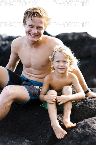 Young man with younger brother (4-5) sitting on rocks