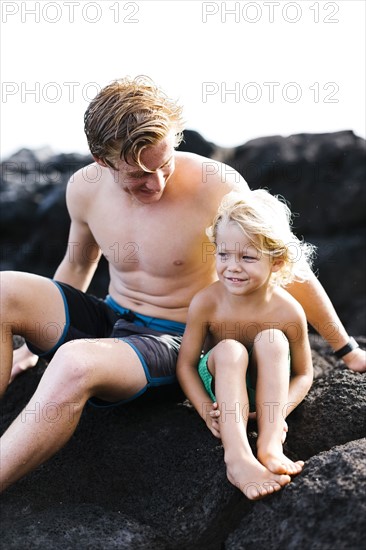 Young man with younger brother (4-5) sitting on rocks