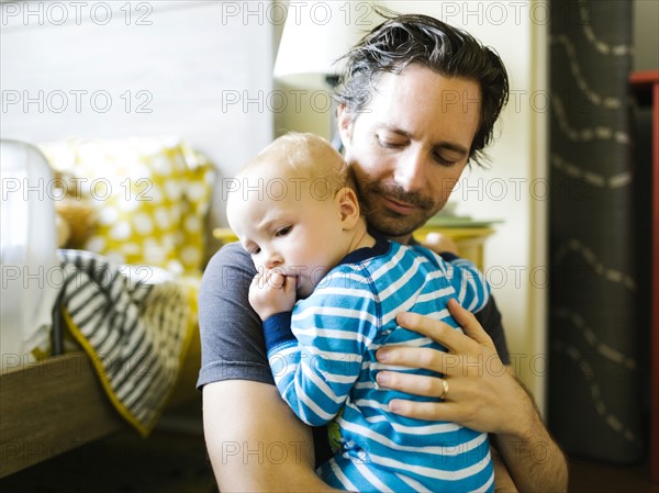 Father embracing baby boy (12-17 months) in bedroom