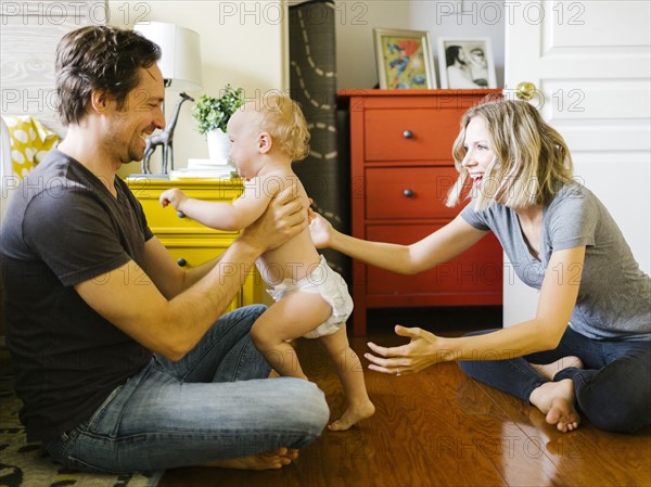 Baby boy (12-17 months) taking first steps with parents at home