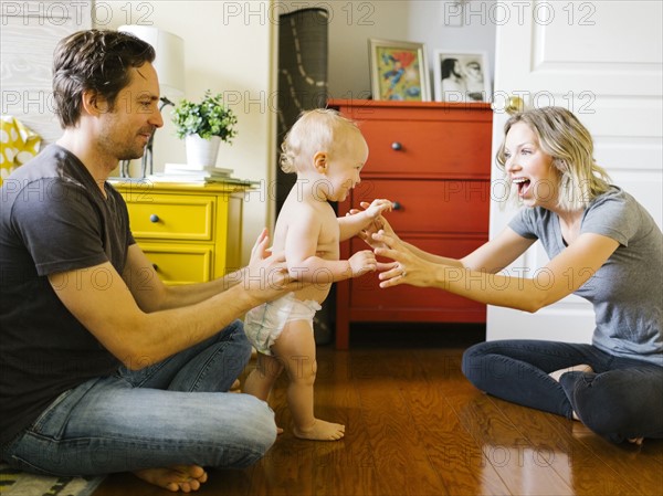 Baby boy (12-17 months) taking first steps with parents at home