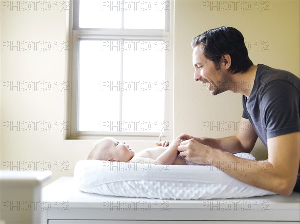 Father playing with baby boy (12-17 months) on changing mat