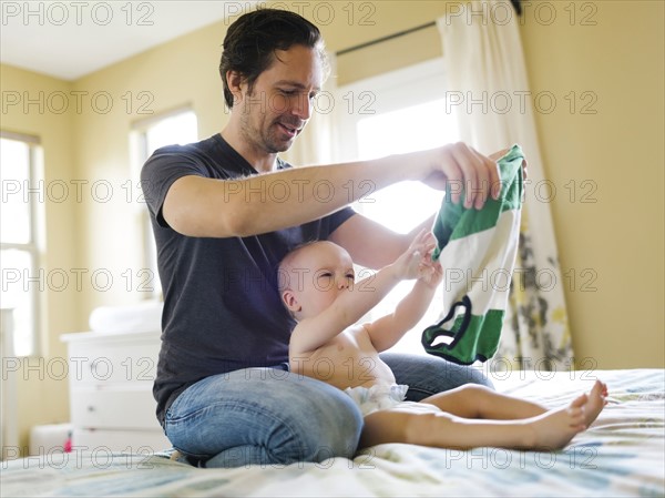 Father dressing son (12-17 months) in bedroom