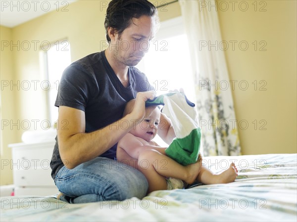 Father dressing son (12-17 months) in bedroom