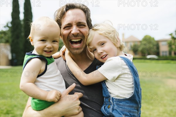 Portrait of father carrying sons (12-17 months, 4-5) in park