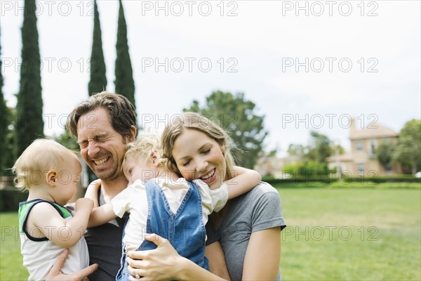 Parents with sons (12-17 months, 4-5) embracing in park