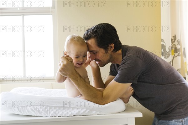 Father playing with baby boy (12-17 months) on changing mat
