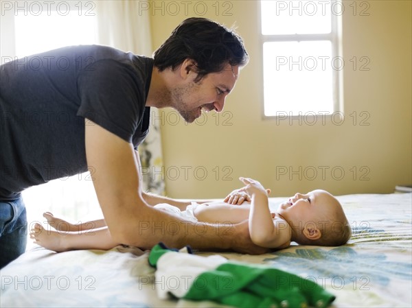 Father dressing son (12-17 months) in bedroom