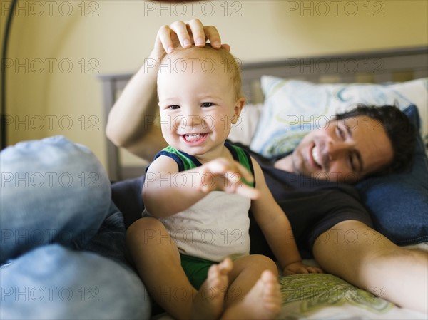Father stroking baby boy (12-17 months) in bedroom
