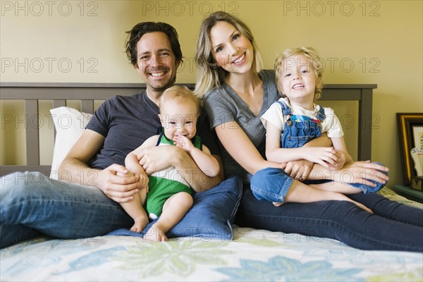 Portrait of parents sitting with sons (12-17 months, 4-5) on bed