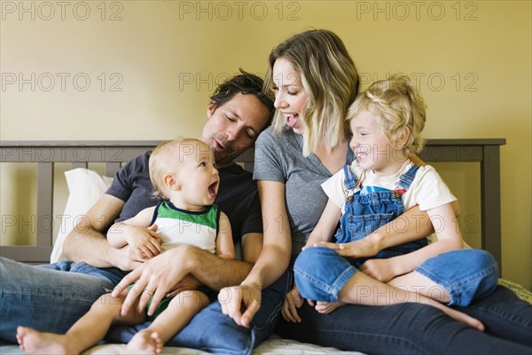 Parents playing with sons (12-17 months, 4-5) on bed