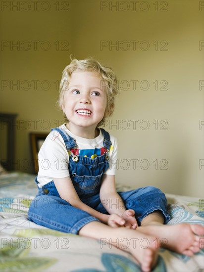 Smiling boy (4-5) sitting on bed and looking away