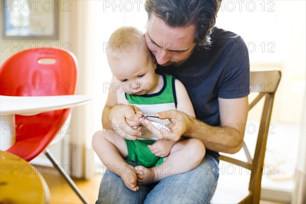 Father cutting son's (12-17 months) fingernails