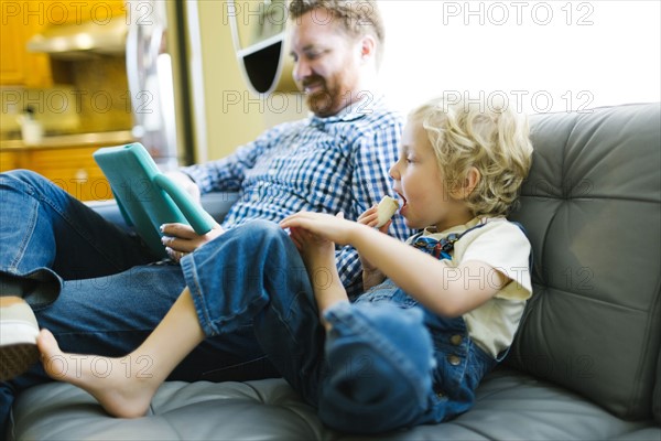 Boy (4-5) and man using digital tablet on sofa in living room