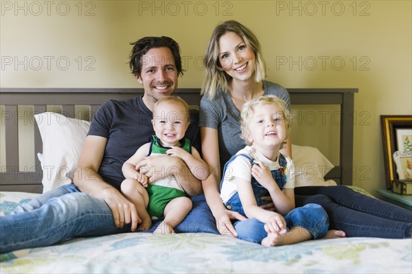 Portrait of parents sitting with sons (12-17 months, 4-5) on bed