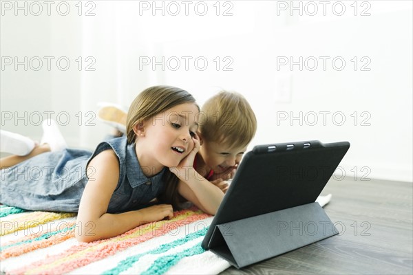 Siblings (2-3, 6-7) lying down on carpet and watching digital tablet