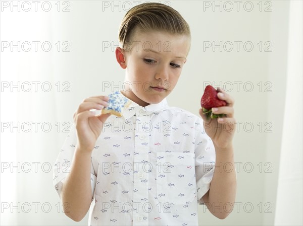 Boys (6-7) holding strawberry and cookie in hands