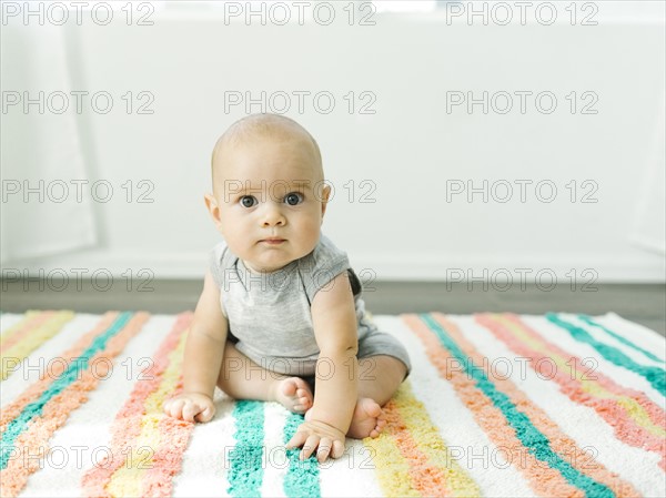 Portrait of baby boy (6-11 months) sitting on colorful carpet