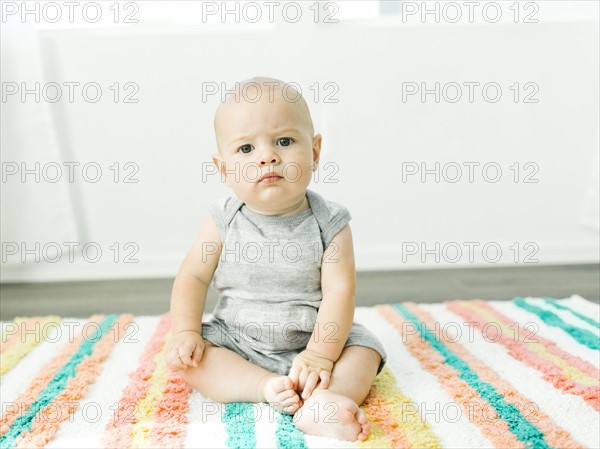 Portrait of baby boy (6-11 months) sitting on colorful carpet