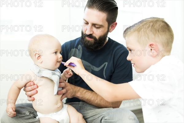 Father looking at boy (6-7) feeding brother (6-11 months)