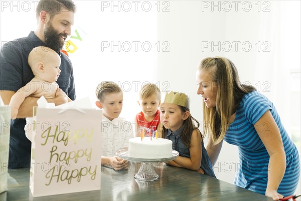Parents with children (6-11 months, 2-3, 6-7) looking at daughter (6-7) blowing birthday candles