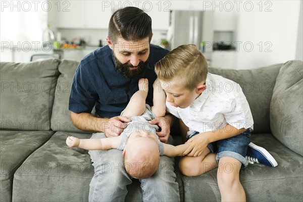 Father and boy (6-7) playing with baby boy (6-11 months) in living room