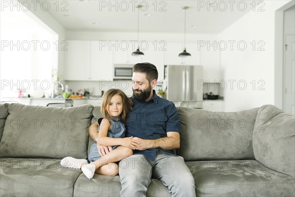 Father with daughter (6-7) sitting on sofa in living room