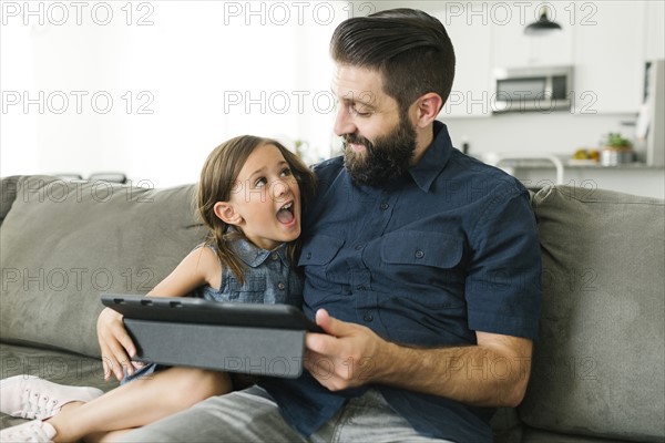 Father with daughter (6-7) using digital tablet in living room