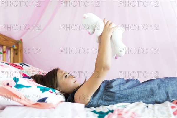 Girl (6-7) playing with teddy bear in bedroom