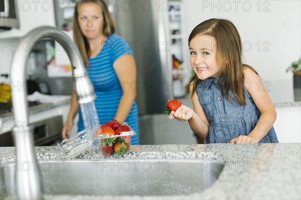 Mother looking at daughter (6-7) holding strawberry in kitchen