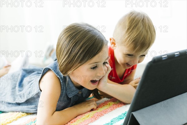 Siblings (2-3, 6-7) lying down on carpet and watching digital tablet