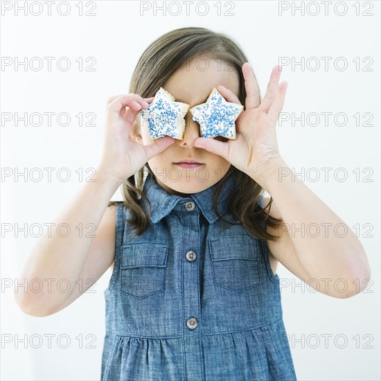 Girl (6-7) holding cookies in front of eyes