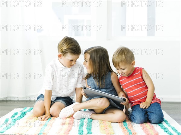 Children (2-3, 6-7) sitting on rug with digital tablet