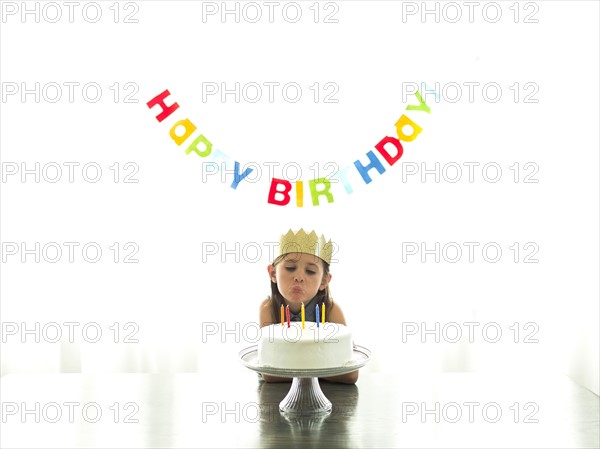 Girl (6-7) in paper crown blowing candles on birthday cake