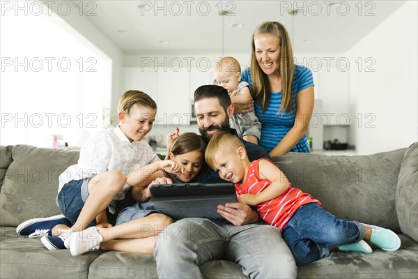 Family with four children (6-11 months, 2-3, 6-7) using digital tablet